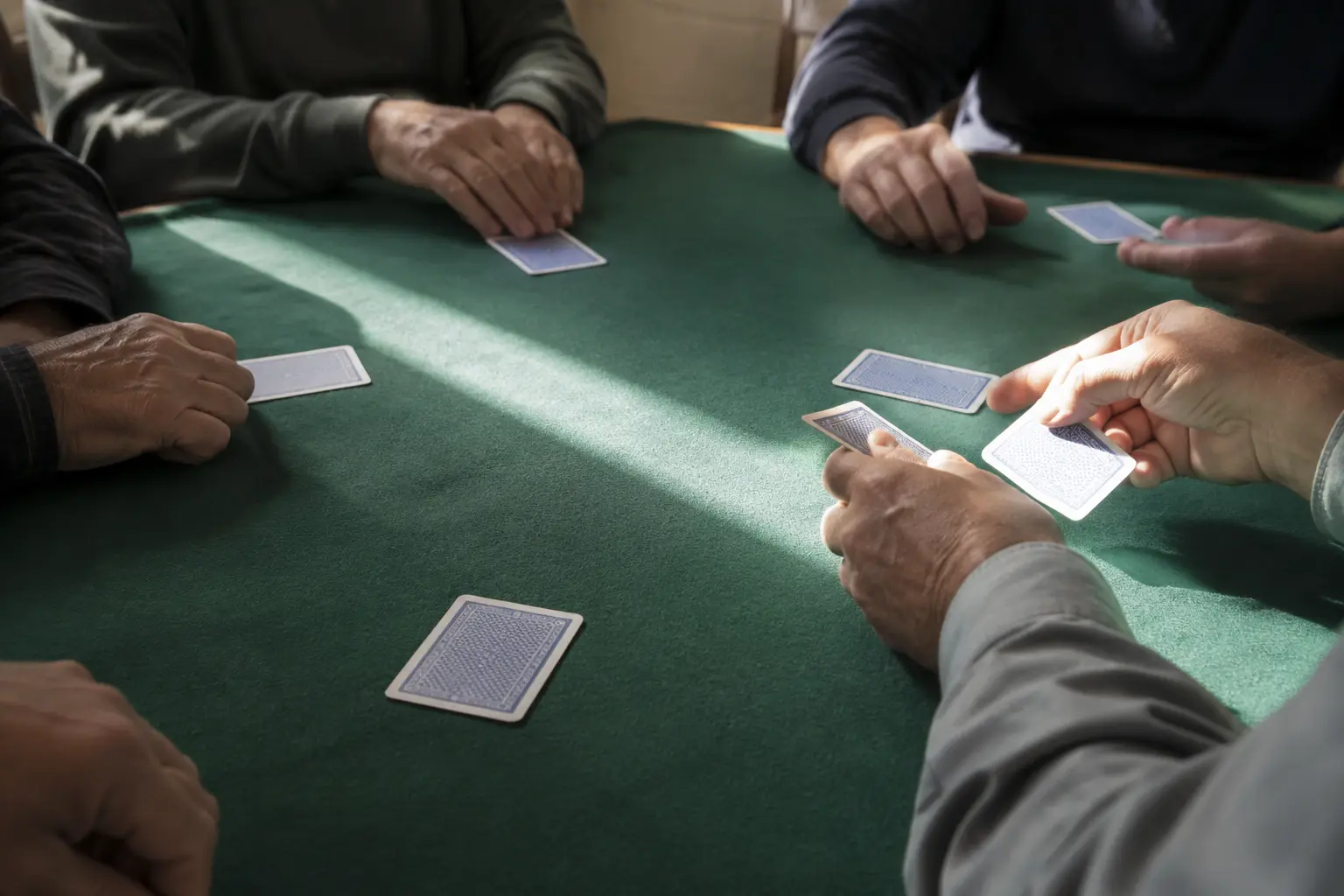 Adult hands dealing blank face-down cards around a modest community poker table